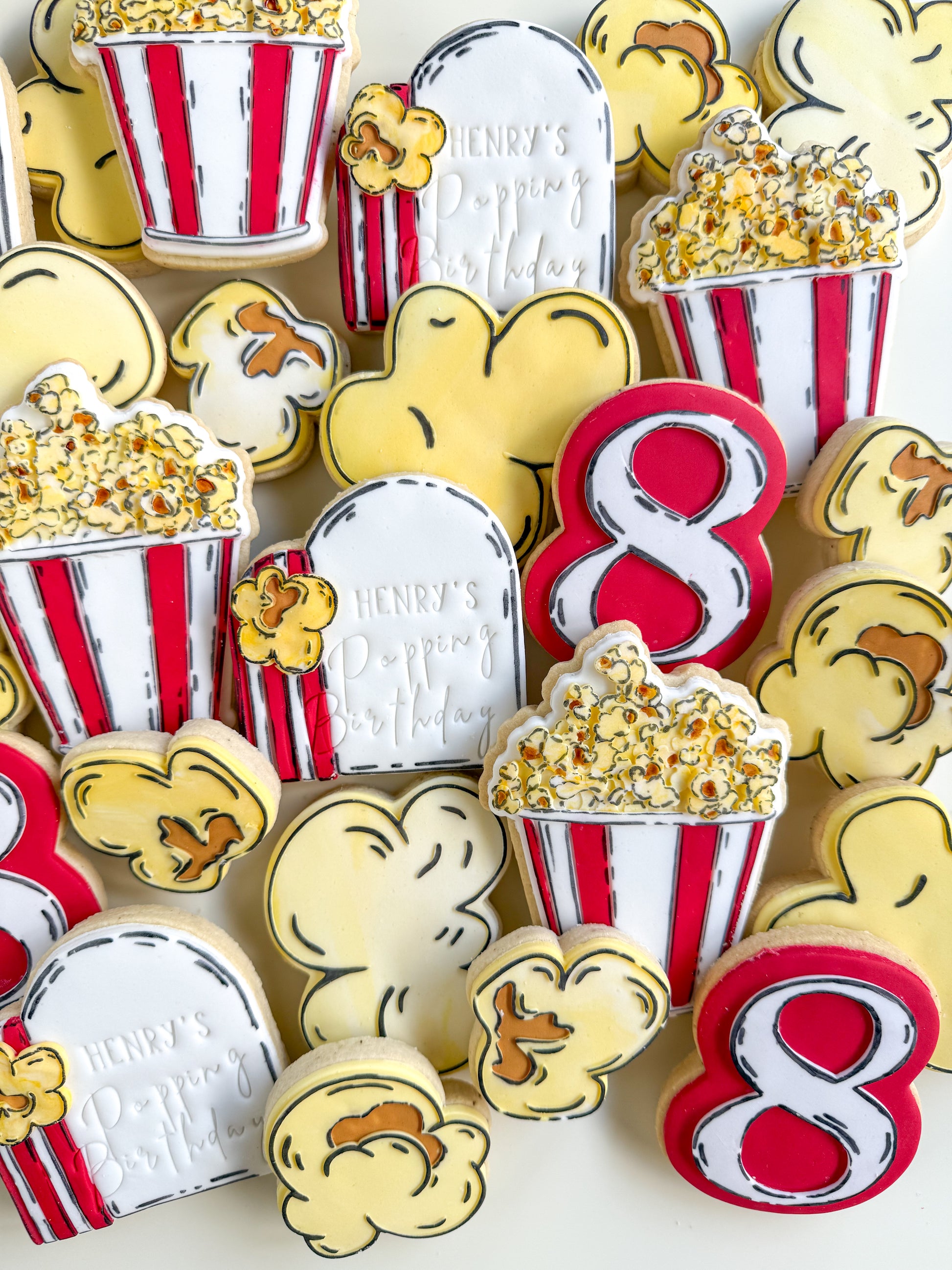 Decorative cookies shaped like popcorn buckets and number 8s on a white background