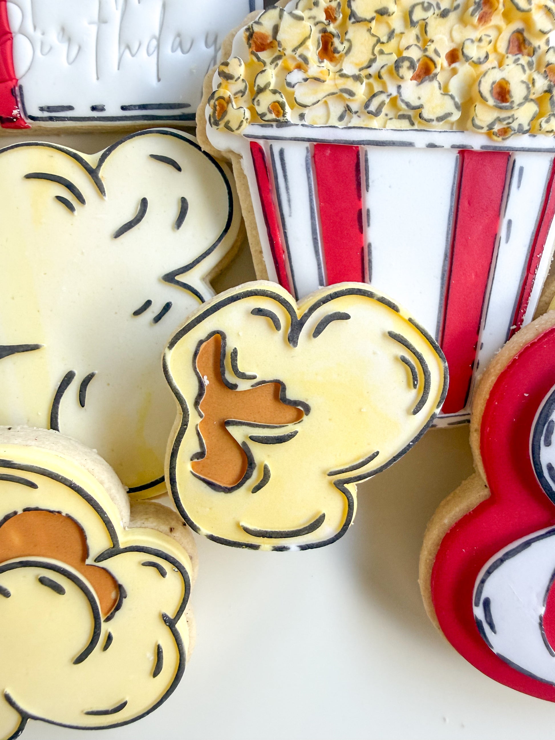 Decorative cookies shaped like movie theater seats and popcorn, with a box of popcorn in the background.